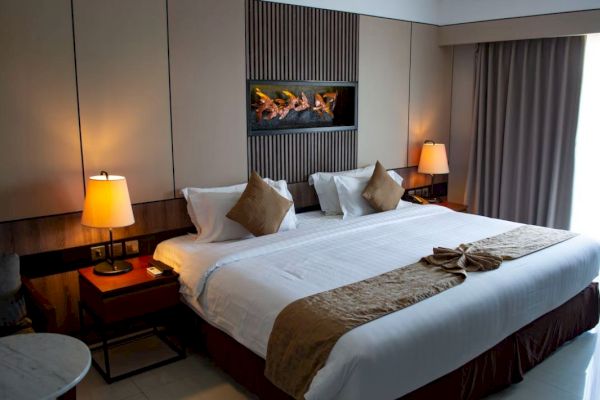 The image shows a hotel room with a large bed, pillows, bedside tables with lamps, and a decorative feature on the wall.