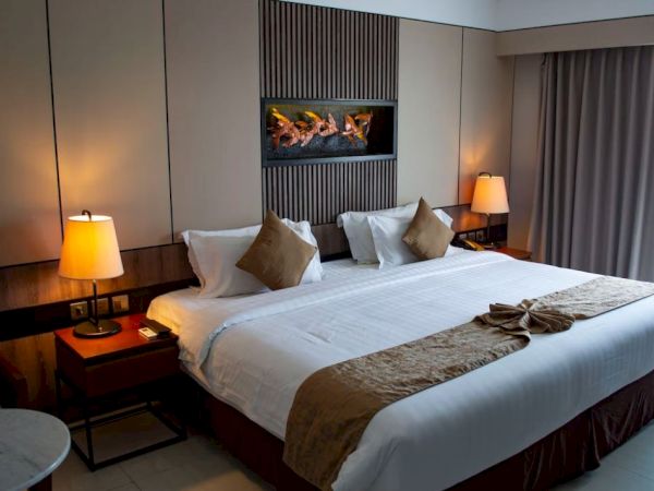 The image shows a hotel room with a large bed, pillows, bedside tables with lamps, and a decorative feature on the wall.