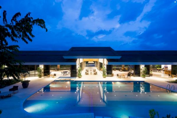 A luxurious building at night with a large, illuminated swimming pool reflecting the structure, under a dramatic blue sky.