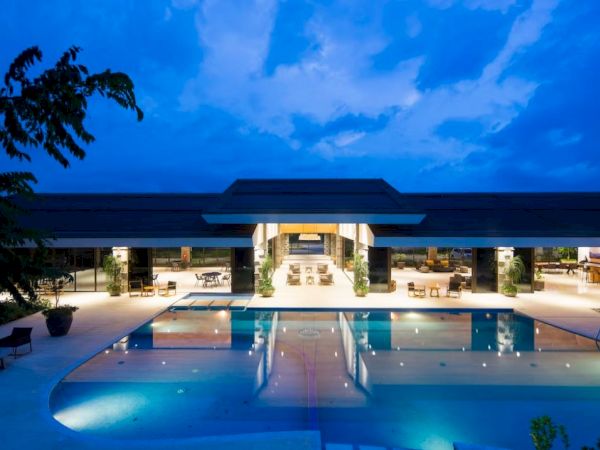 A luxurious building at night with a large, illuminated swimming pool reflecting the structure, under a dramatic blue sky.