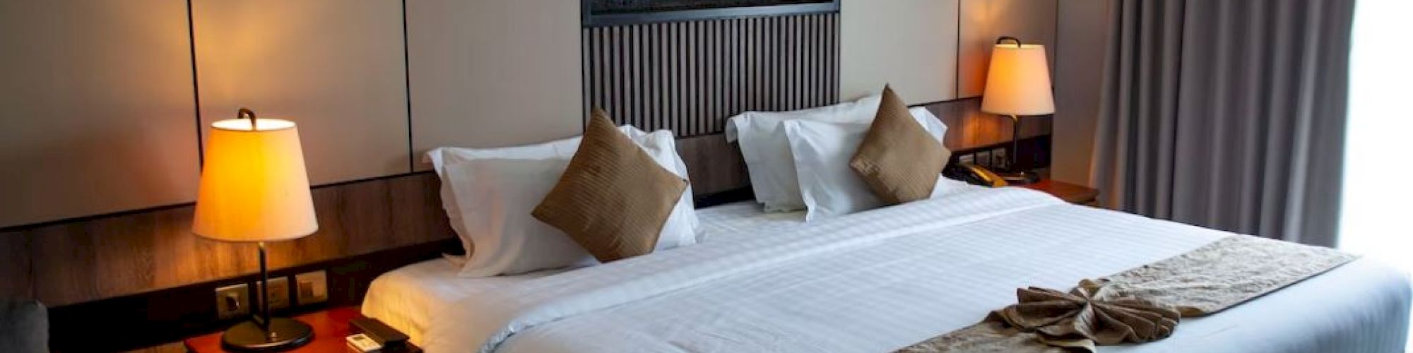 A neatly arranged hotel room with a large bed, decorative pillows, bedside lamps, and wall art. The room feels cozy and inviting.