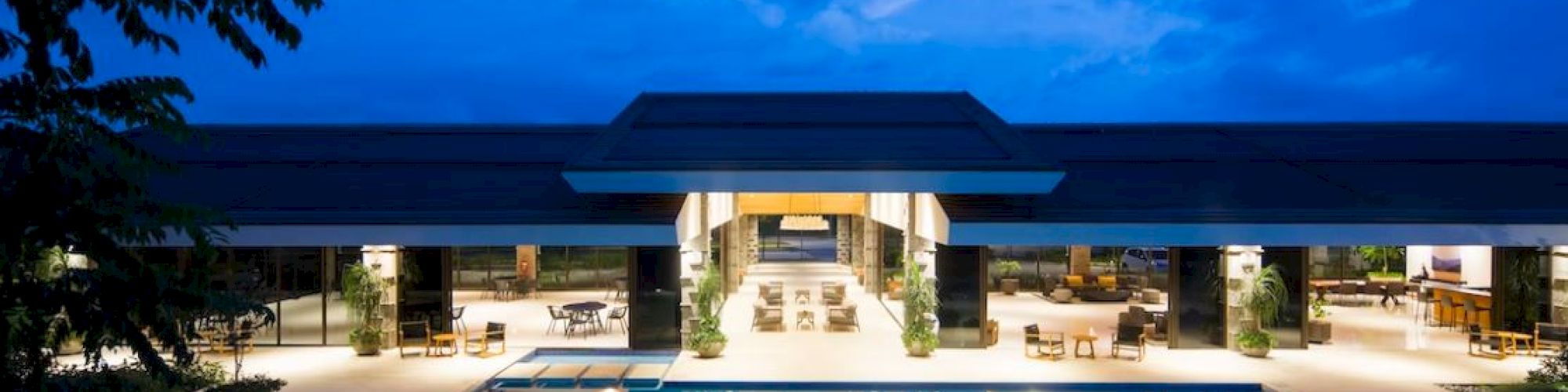 A luxurious outdoor pool area at night, with elegant lighting and a modern building in the background, under a vibrant blue sky.