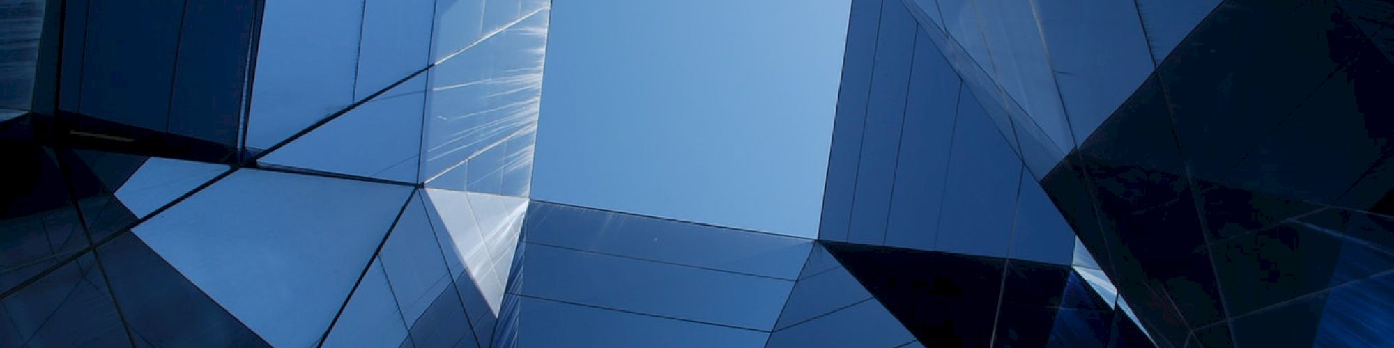 Abstract view of modern glass architecture with a clear blue sky in the center, creating geometric reflections and light patterns.