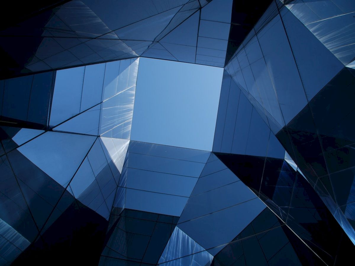 The image shows a geometric view of modern glass buildings with blue reflective surfaces, creating an abstract pattern looking upwards.
