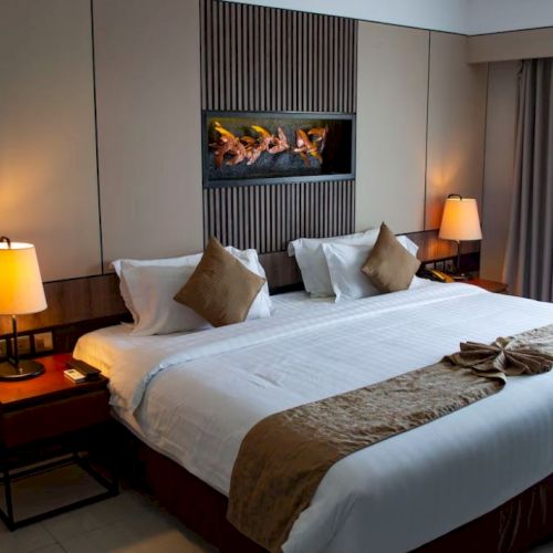 A cozy hotel room with a large bed, bedside tables with lamps, and a wall feature. Curtains cover a window, enhancing the ambiance.