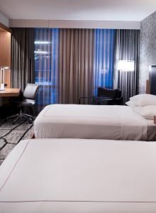 The image shows a modern hotel room with two beds, a TV, a desk, and stylish decor, creating a comfortable atmosphere.