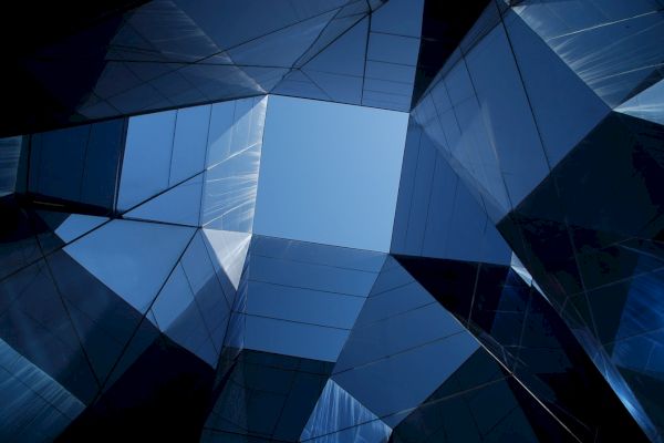 A geometric perspective of modern architecture with glass and metal reflections, creating a symmetrical pattern towards an open sky.