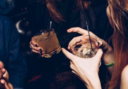 People enjoying drinks together, chatting and smiling in a lively atmosphere, with a focus on their hands and beverages.