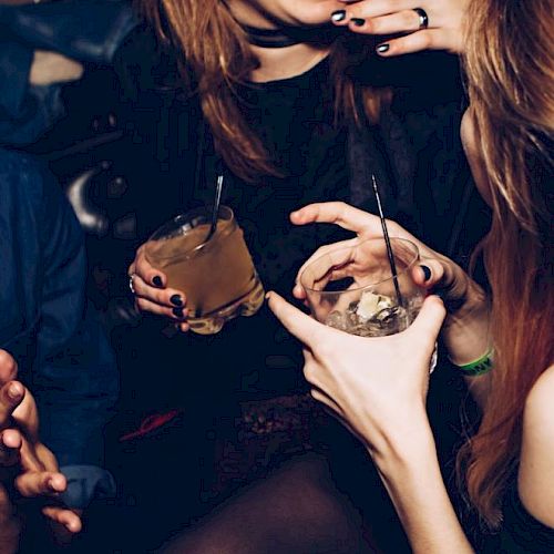 People enjoying drinks together, chatting and smiling in a lively atmosphere, with a focus on their hands and beverages.