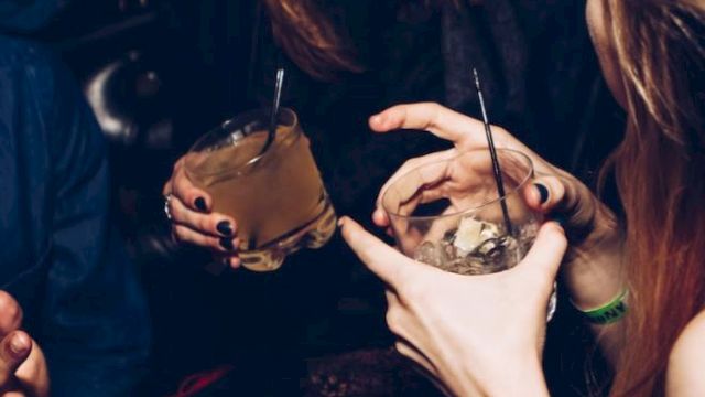 People enjoying drinks together, chatting and smiling in a lively atmosphere, with a focus on their hands and beverages.