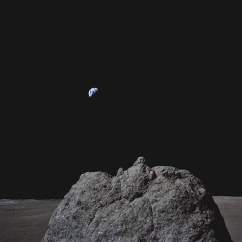 A rocky lunar surface with Earth rising in the distant, dark sky, creating a striking space view.