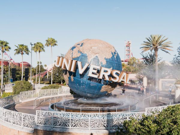 The image shows the iconic Universal globe with palm trees and clear blue sky in the background at a theme park entrance.