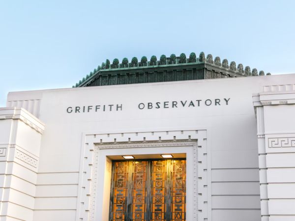 The image shows the entrance of the Griffith Observatory, featuring its name on the building and an ornate door below.
