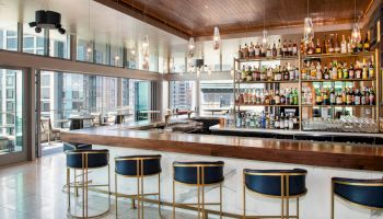 A modern bar with stylish seating, a stocked bar, and large windows for a city view.