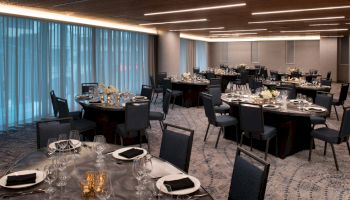 The image shows an elegantly set banquet hall with round tables, chairs, plates, glasses, and napkins.