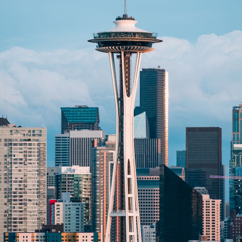 The image shows the Space Needle with a city skyline in the background, under a clear sky.