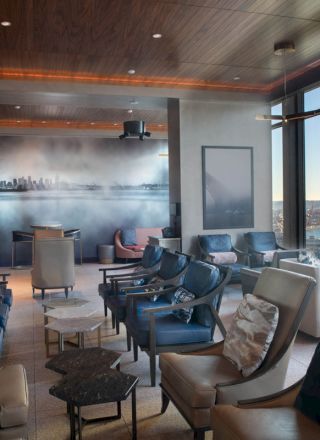 A modern lounge with plush seating and large windows offering a waterfront view, featuring a mural on the back wall.