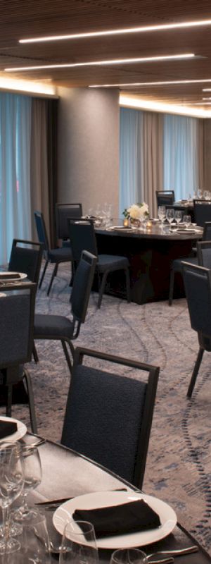 A banquet hall is set up with round tables, chairs, elegant place settings, and soft lighting for an event.